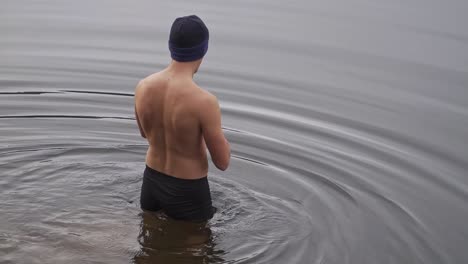 man walking into cold water wearing only swimming trunks and knit cap. onsen, cold water therapy, polar plunge concept.