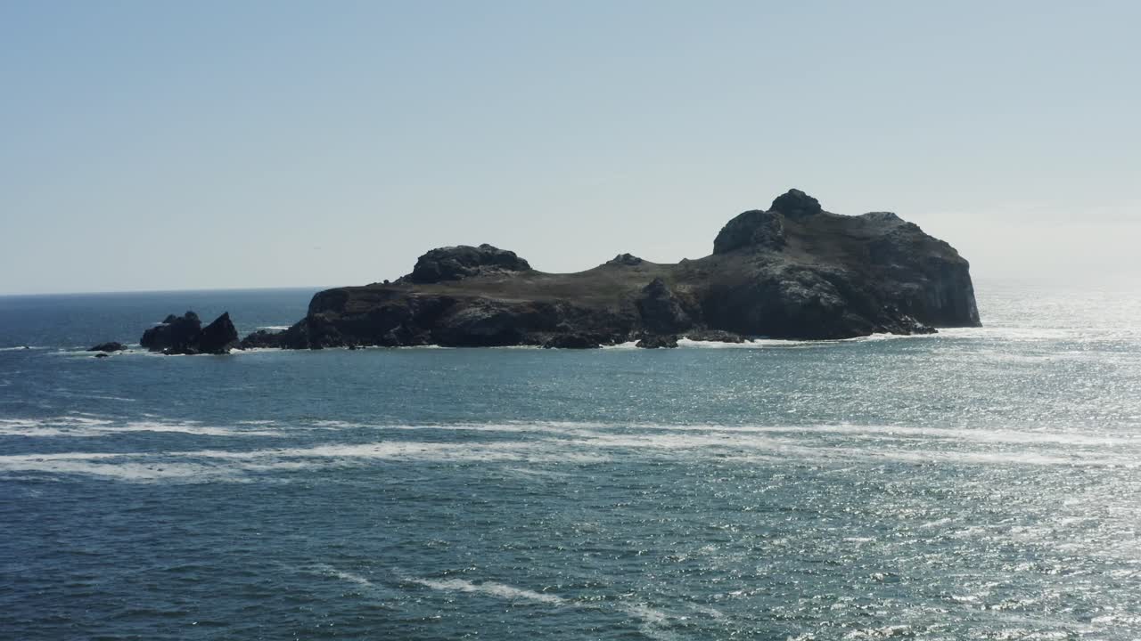 Maestose riprese aeree con drone, che si muovono lentamente verso un enorme masso nell'Oceano Pacifico, circondato da onde che si infrangono, Oregon.