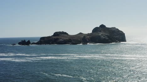 Majestic-aerial-drone-footage,-slowly-tracking-toward-a-very-large-Pacific-ocean-boulder-which-is-surrounded-by-crashing-waves,-Oregon