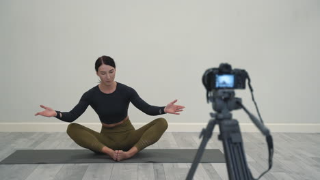 yoga at home. woman explaining lotus pose (padmasana), recording a video tutorial, looking at a camera