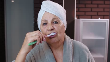 senior woman grandmother with towel brushing teeth and looking into a mirror after shower at home