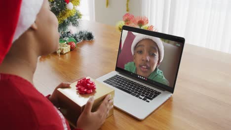 mujer afroamericana con sombrero de santa usando una computadora portátil para una videollamada de navidad, con un niño en la pantalla