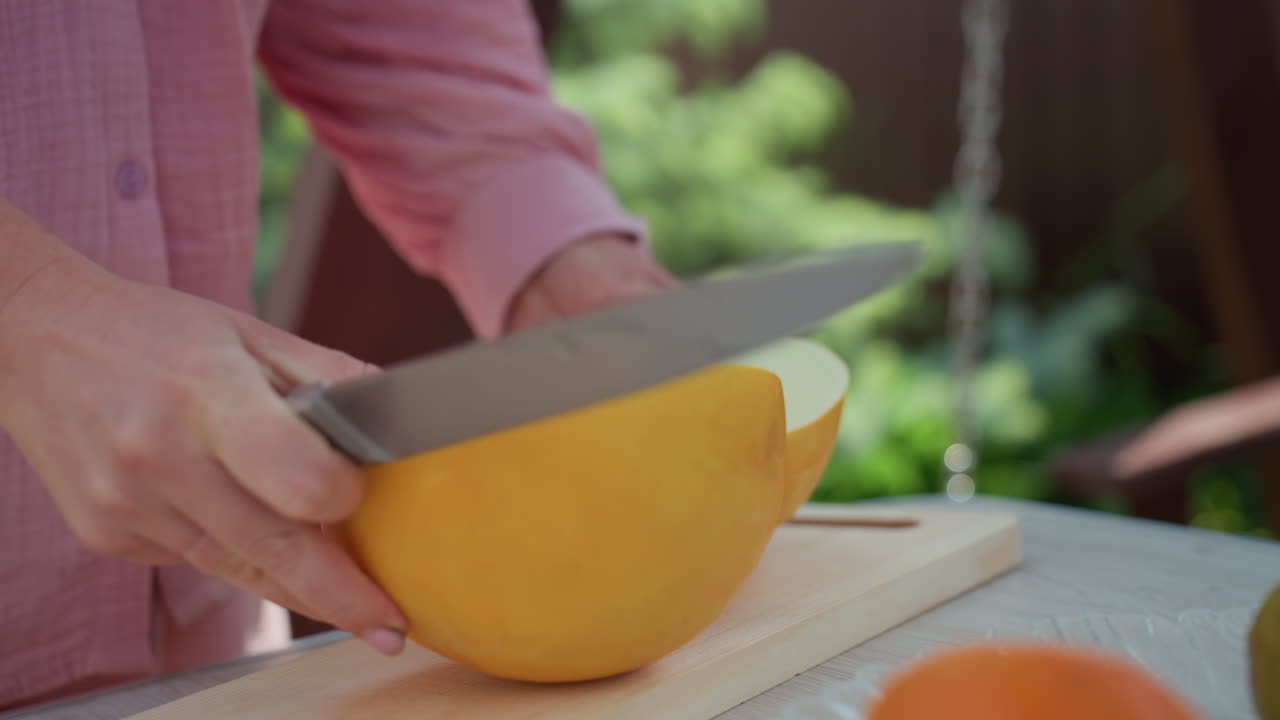 Woman Cuts Melon, Woman Slicing Yellow Melon In Summer Sunlight, Casual Woman Preparing Fresh Fruit On Picnic Table, Closeup Of Woman Slicing Ripe Melon With Nearby Fruits In Warm Outdoor Setting