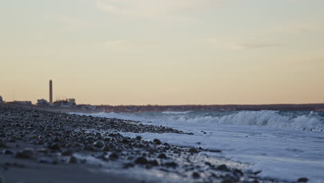 wide shot of waves crashing on a beach during golden hour with power station in background