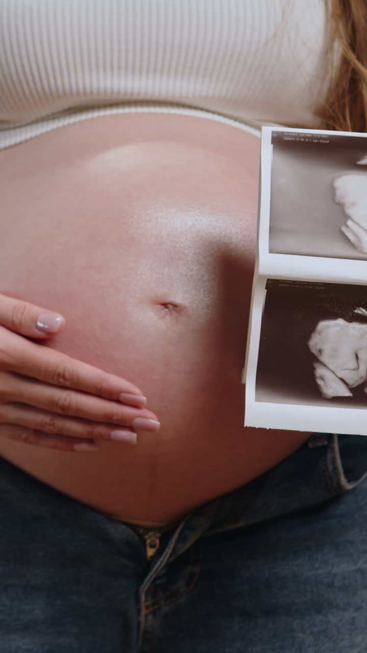 Primo piano del ventre di una donna incinta che mostra una foto di un'ecografia mentre indossa abiti casual