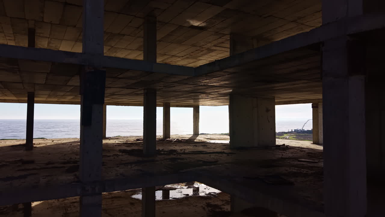 La luce del sole filtra attraverso i piani vuoti di un edificio abbandonato, rivelando ombre e riflessi in uno spazio dimenticato che si affaccia sull'orizzonte.