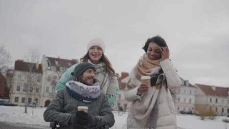 disabled man in wheelchair and two women walking and talking together in the city in winter 1