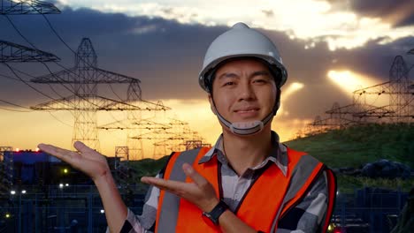 close up of asian male engineer with safety helmet smiling and pointing to side while standing near high voltage tower