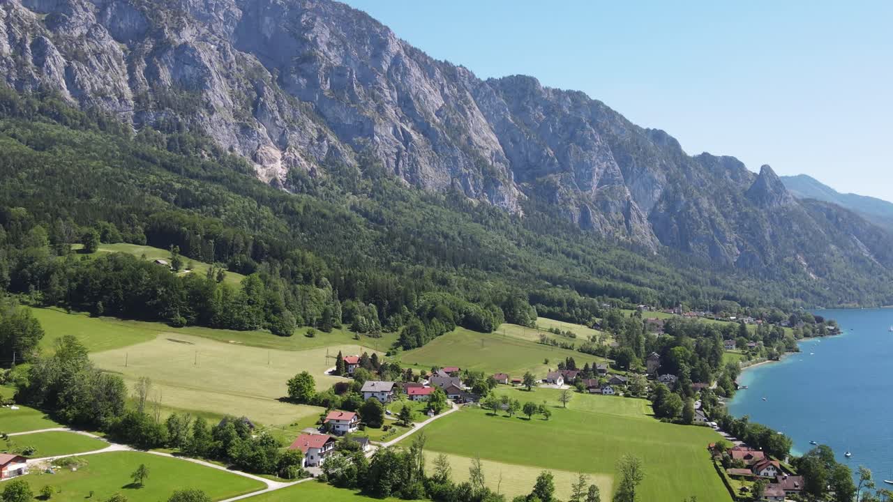 Il lago Attersee in Austria, nella regione alpina del Salzkammergut. Vista aerea da drone del villaggio sul lago, dei campi verdi e delle pendici montuose mozzafiato lungo un limpido lago alpino.