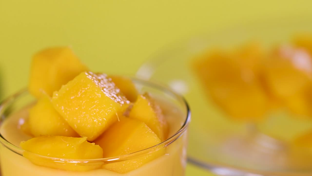 Una mano posiziona con cura cubetti di mango giallo brillante su una guarnizione di frullato di frutta denso
