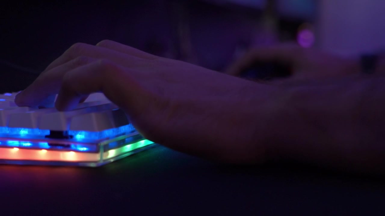 Primo piano della mano di una persona che gioca a videogiochi per PC su una tastiera LED multicolore in un internet café