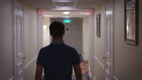 young man in blue shirt walking along corridor at hallway hotel back view