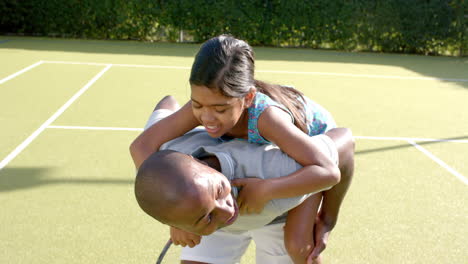 playing together, father giving daughter piggyback ride on tennis court, smiling