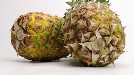 two whole juicy yellow tropical pineapples falling and bouncing on white table top in slow motion