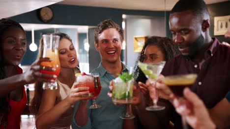 grupo de jóvenes amigos que se reúnen para tomar bebidas en un bar de cócteles y hacer un brindis