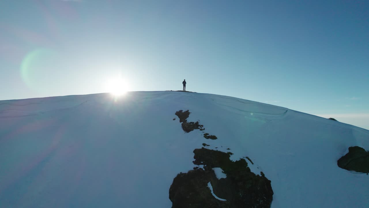 una persona está de pie en una montaña nevada, con el sol posicionado detrás de ellos, en francia