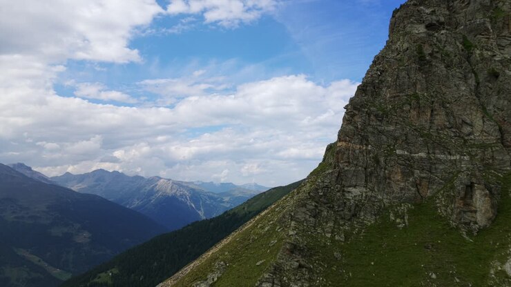 Majestätischer felsiger Berggipfel, zerklüftete Klippen und grüne Hänge unter blauem Himmel mit Wolken, Umbrail-Pass, Schweizer Alpen, Schweiz. Luftaufnahme mit einer Drohne