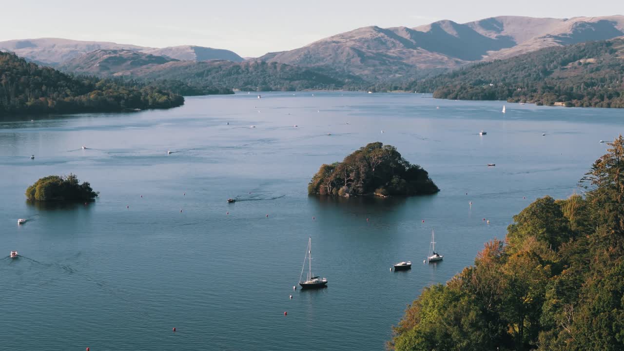 Aerial left orbit through trees revealing Lake Windermere with boats, summer sky