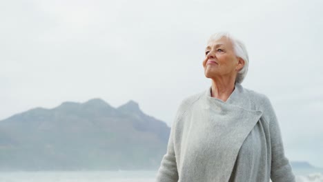 Senior-woman-standing-with-hands-raised-on-beach