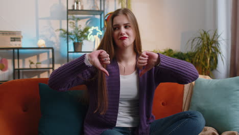 upset young woman showing thumbs down, dislike bad work, disapproval, dissatisfied feedback at home