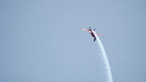 aerobatic stunt plane performs roll maneuver in the sky leaving white smoke trail