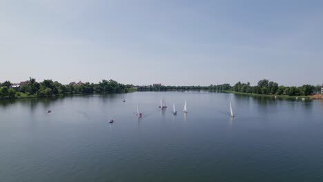 Sailboats-sail-on-a-lake,-distant-drone-dolly-zoom-in-shot