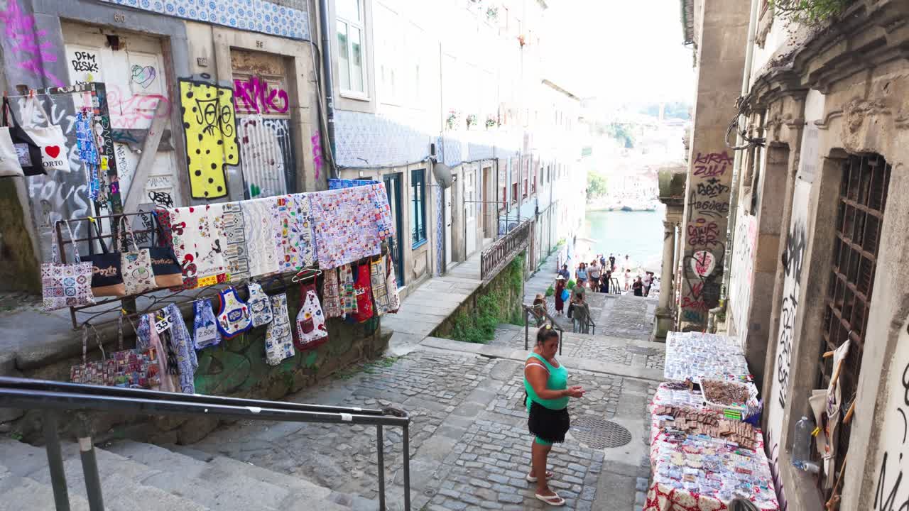A woman browses handmade goods on a cobblestone street leading to Porto's Luís I Bridge.