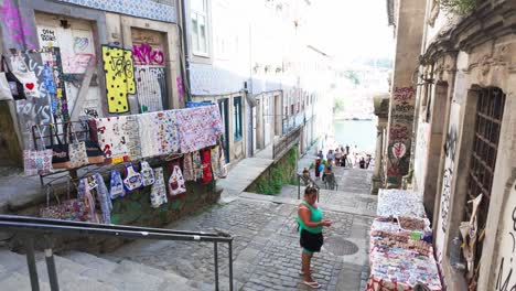 a woman browses handmade goods on a cobblestone street leading to porto's luís i bridge.