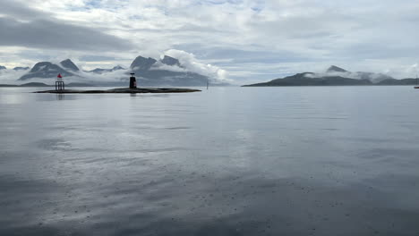 Toma-Panorámica-De-Un-Asombroso-Paisaje-Marino-Tranquilo-Con-Montañas-Cubiertas-De-Nubes-Y-Cielo,-Islas-Y-Balizas-De-Luz-En-La-Costa-De-Noruega