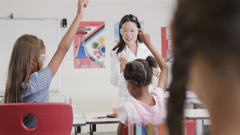 diverse female teacher and girls raising hands in elementary school chemistry class, slow motion