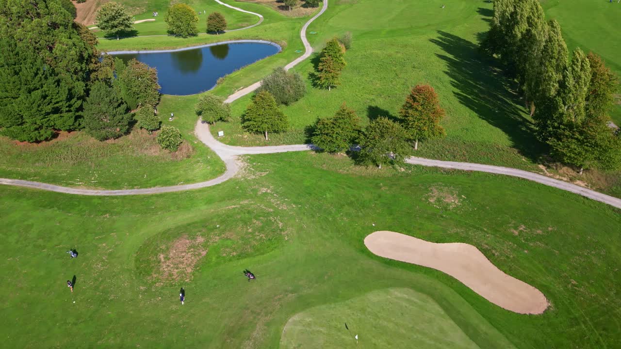Drone aerial view of a golf course in France showing greens, sand bunkers, ponds, trees, and walking paths under sunlight