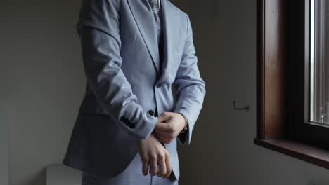 groom adjusting his suit sleeves near a window, preparing for his wedding day