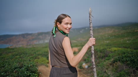 outdoor woman going hill on summer day. smiling hiker turning camera hold stick