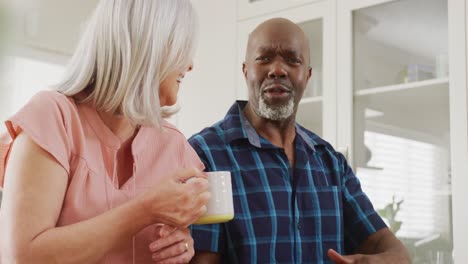 Happy-senior-diverse-couple-sitting-in-living-room-and-drinking-coffee