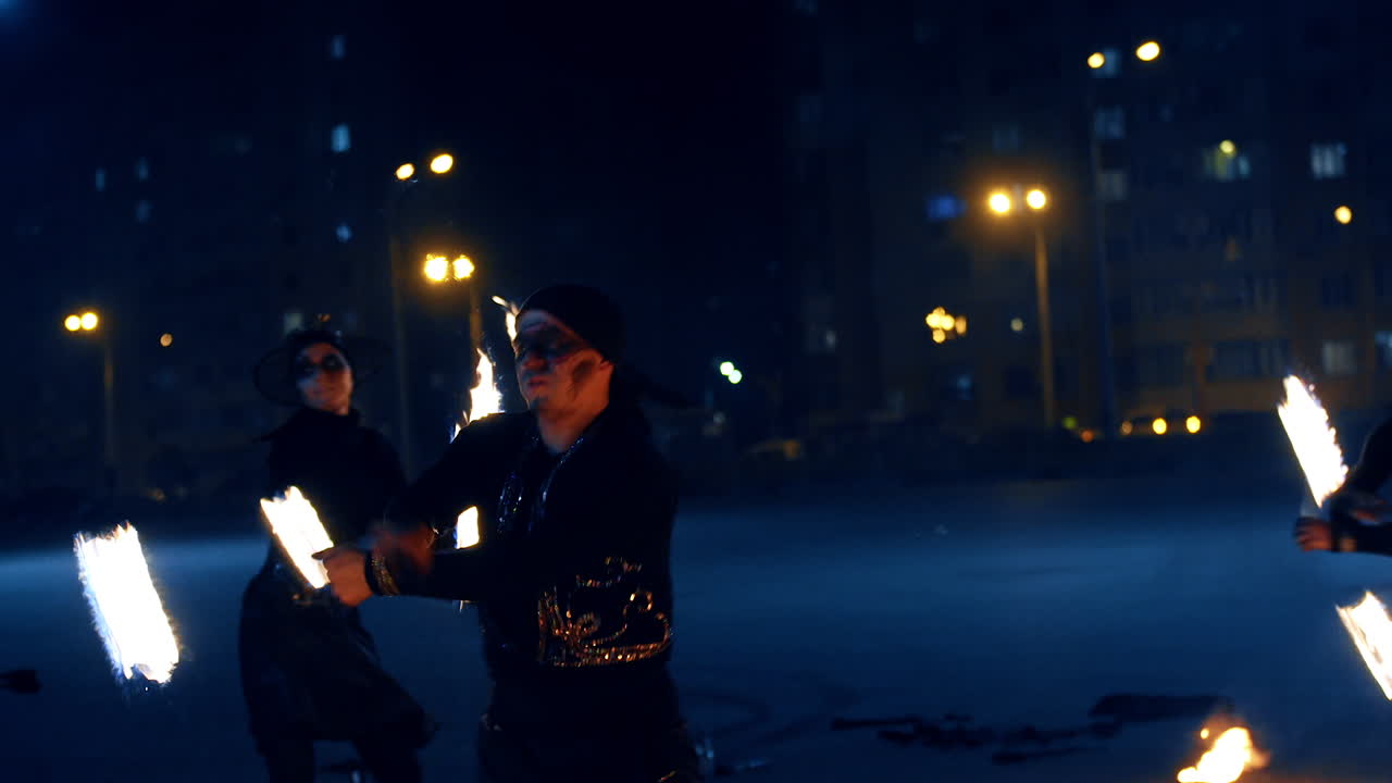 Man and woman in black costumes and dark make up showing the fire spectacle. Actors present fire show.