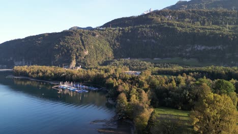 A-beautiful-panoramic-view-over-the-Walensee-Lake-with-serene-blue-water,-a-small-marina-with-sailboats-and-sun-soaked-trees-on-the-mountain-hills
