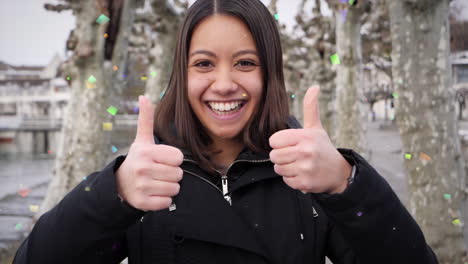 Portrait-of-excited-young-woman-celebrating-under-confetti-shower-in-wintry-landscape