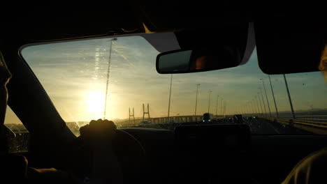 driving across iconic vasco da gama bridge during golden hour sunset, capturing multiple scenic perspectives from inside car with lisbon's urban landscape unfolding