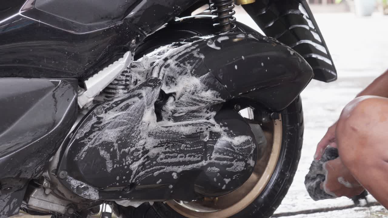 Soapy hands washing the undercarriage of a motorcycle