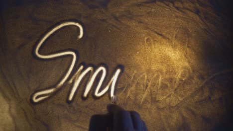 smile inscription. sand on the illuminated glass