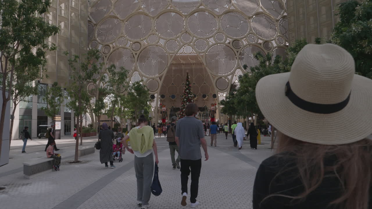 People Walking Through a Modern City Street with a Christmas Tree
