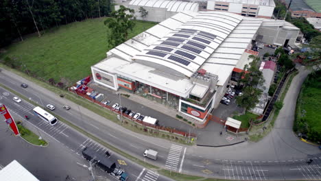 Vista-Aérea-De-Un-Centro-Comercial-Con-Autos-Pasando-Y-El-Dron-Choca-Accidentalmente-Contra-Un-árbol-Alto