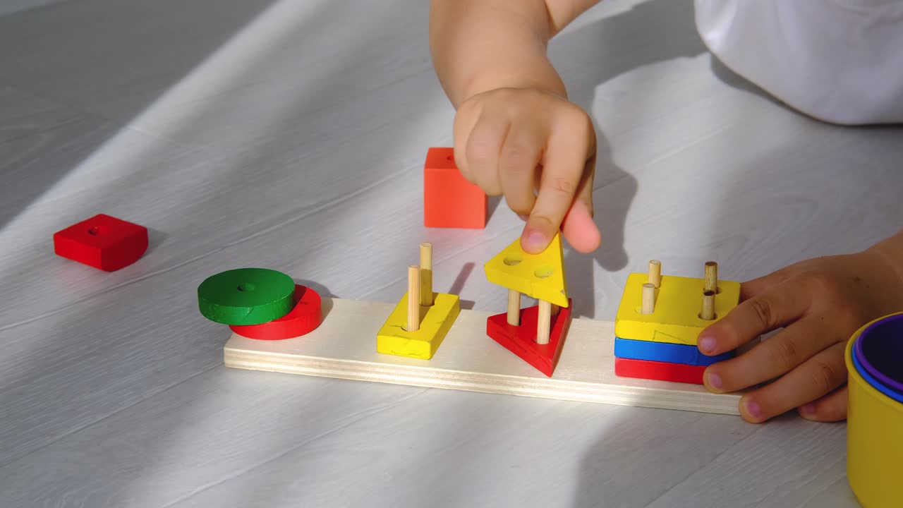 primer plano del niño es las manos doblan un juguete lógico de madera. el bebé recoge una pirámide de madera. juguetes lógicos educativos para niños. juegos montessori para niños