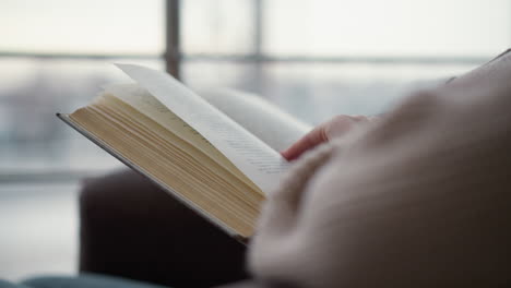 close-up of an open book with gently turning pages, soft natural light, and blurred glass panel background, cozy reading atmosphere, warm tones, and delicate hand movement