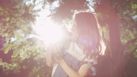 Young-Caucasian-woman-in-glasses-holding-small-cat-and-kissing-it-in-the-park-on-a-summer-day