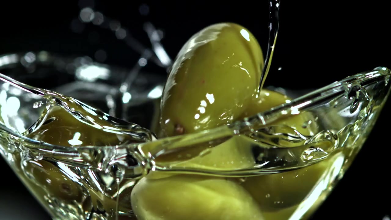 Olive verdi che cadono nell'olio d'oliva in una ciotola di vetro
