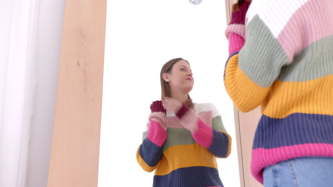 Smiling woman in colorful sweater looking at herself in large mirror