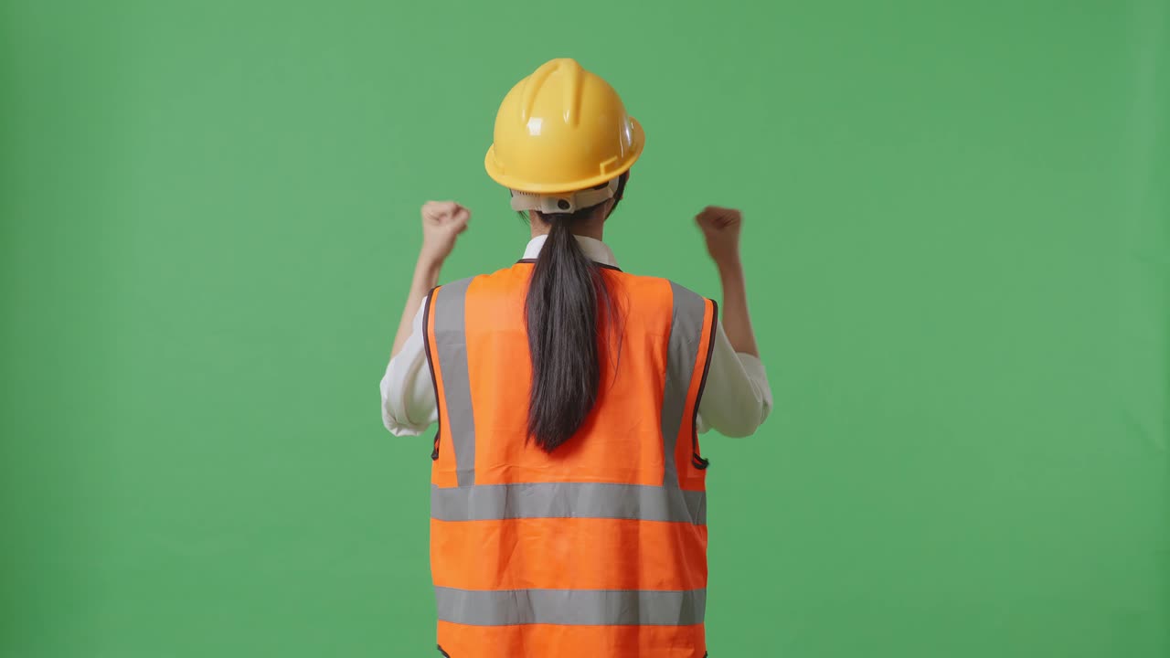 안전 헬 을 착용 한 여성 엔지니어 가 녹색 스크린 배경 스튜디오 에서 일 하는 동안 손 을 들어 축하 하는 모습