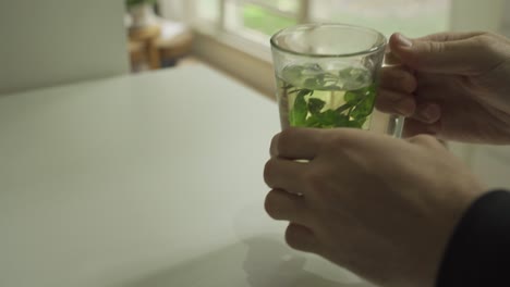 hands holding herbal tea on table in apartment - then man drinks and puts back glass