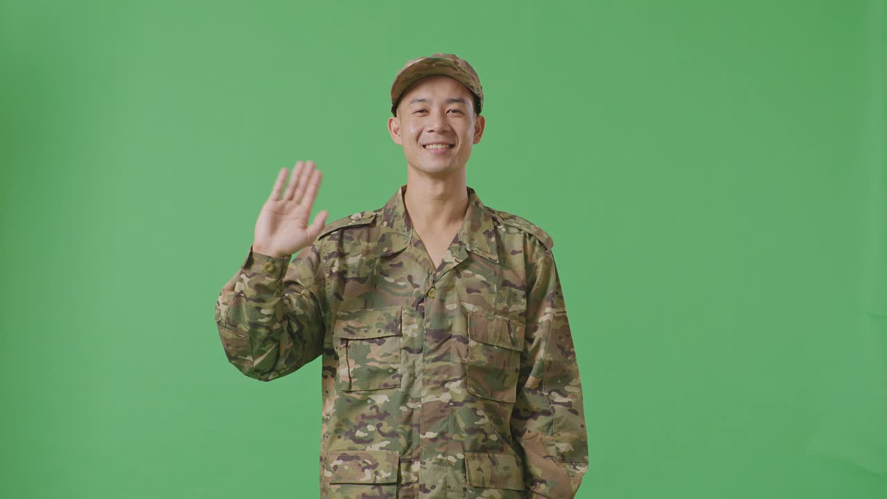 Asian Man Soldier Smiling, Waving Hand, And Saying Bye While Standing In The Green Screen Background Studio